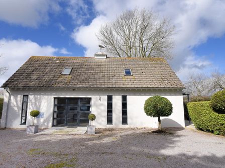 A white building with a tiled roof and three narrow windows with two potted plants and one tree in front at The Water Tower Studio in Seaton Devon