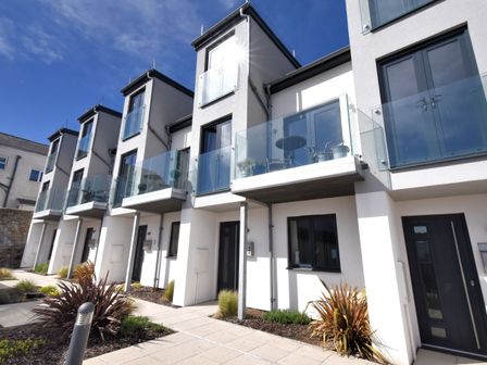A row of modern townhouses with glass balconies and black doors with plants and paved walkway in front at 3 Grove Mews in Seaton Devon