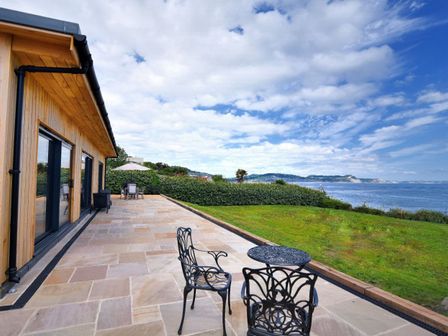 A patio with metal chairs and table next to a lawn overlooking the sea at Harbour Heights Cottage Lyme Regis