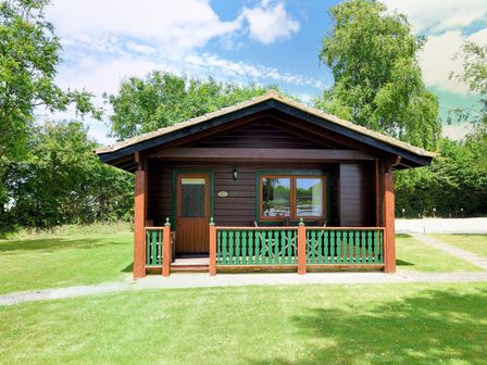 A small wooden cabin with green railings and a brown door surrounded by grass and trees at 4 Pinewood Retreat in Pinewood