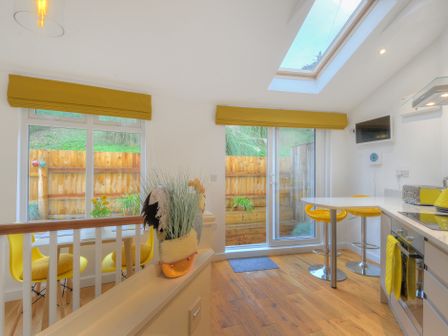 A kitchen with yellow stools and blinds with wooden floor and countertop at Seashore in Lyme Regis
