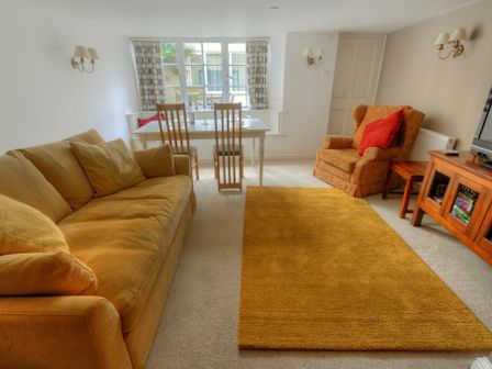 A living room with a yellow sofa a patterned armchair and a wooden dining table with chairs at Tudor Cottage in Lyme Regis