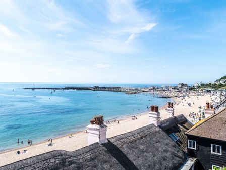 A beach with people on the sand and in the water beside buildings and a harbor at 3 Beach Way House in Lyme Regis