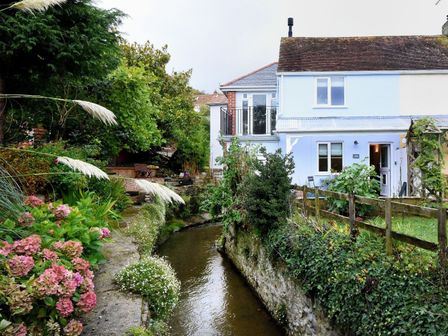 A narrow river flowing beside a house with a garden and plants at 1 Lymbrook Cottages in Lyme Regis