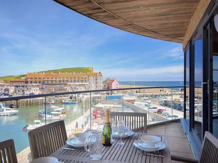A balcony with a wooden dining table and chairs overlooking a harbor with boats and buildings at Venezuela West Bay