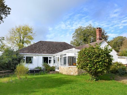 A white single-story house with a conservatory and a garden with outdoor seating at Rooks Acre in Rousdon