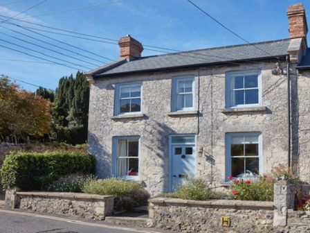 A stone house with two visible chimneys and a blue door and windows with plants in front at Lavender Cottage in Beer