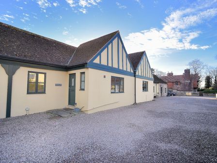 Exterior view of a building with yellow walls and blue trim next to a gravel driveway at 2 Home Farm South in Rousdon