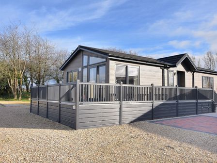 A modern single-story house with large windows and a surrounding gray fence on a gravel yard at Hazelwood 4 @ Pinewood Retreat in Pinewood