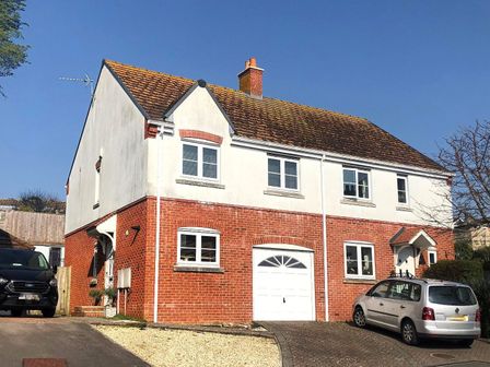A semi detached house with brick and white exterior and two cars parked outside at Annings View in Lyme Regis