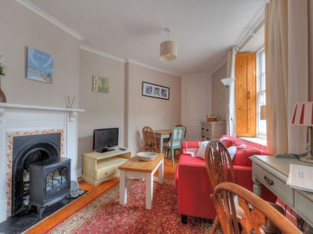 A living room with a red sofa a coffee table a wood stove and a TV at Driftwood in Lyme Regis