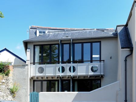 A two-story house with large windows and a balcony with circular cutouts at No 2 26 Broad Street Lyme Regis