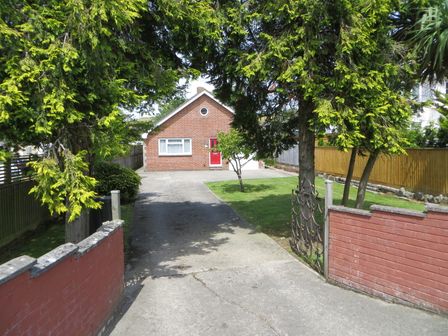 A driveway leading to a single-story brick house with a red door and a small front lawn at Sunny Haven in Preston