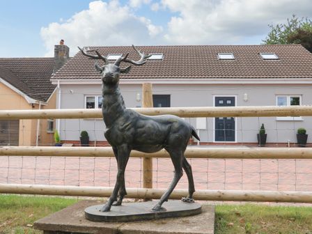 An outdoor scene with a bronze deer statue in front of a wooden fence and houses in the background at Sawtons Cottage 2 in Dawlish