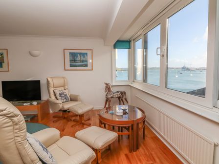 A living room with cream chairs a glass table and a view of the sea at Port View in Falmouth