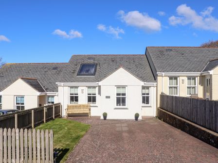 A driveway and grass lawn in front of a white single-story house with a bench outside at Gweal Shortlanesend near Truro