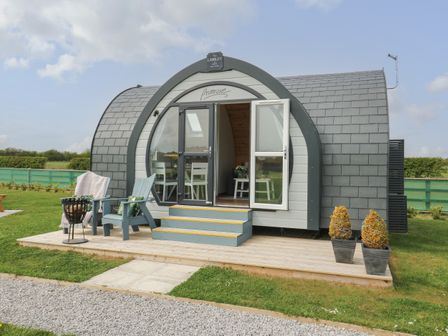 A small curved wooden cabin with steps leading to open glass doors and outdoor chairs on a wooden deck at Primrose Seaton near Hornsea