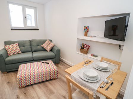 A small living room with a green sofa and matching ottoman a dining table set for two and a wall-mounted TV at Ty Capel Bach in Rachub