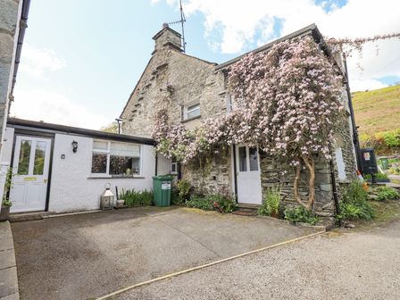 Exterior view of a stone cottage with flowering plants climbing on the walls and two white doors at Yanway Cottage in Troutbeck near Troutbeck Bridge