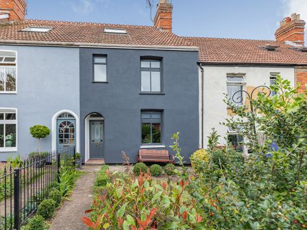 A terraced house with a dark gray front wall and garden with shrubs and a bench at 7 Severn Terrace in Watchet