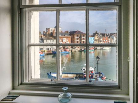 A window looking out onto a harbor with fishing boats and buildings at Embassy Brewers Quay Harbour