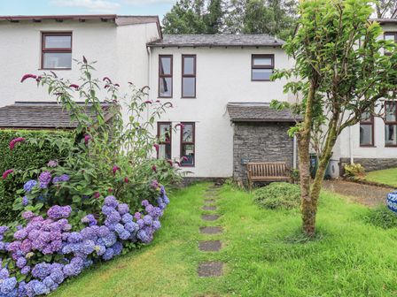 A garden path with stepping stones leading to a white house with flowers a wooden bench and a tree at Merry Bank in Ambleside