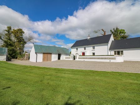 A white house with a red door and detached garage on a gravel driveway with green lawn and trees at Yew Tree House Enniscorthy County Wexford