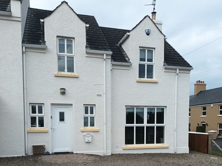 Exterior view of a white house with multiple windows a white door and gravel ground at Stillwaters in Bushmills County Antrim