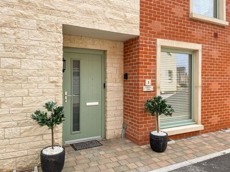 The front entrance of a house with a green door and a window beside it with plants in black pots on a paved area at Sea Gem in Castletown Portland