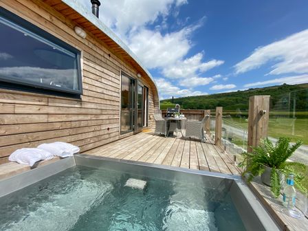 An outdoor wooden deck with a hot tub towels and table with chairs overlooking a grassy landscape at Low Longlands in Cartmel
