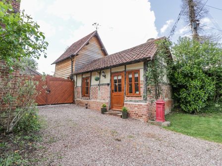 A cottage with a tiled roof wooden door wooden windows and a gravel driveway with plants and a red postbox at The Forge in Tarrington near Bartestree