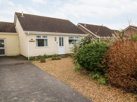 A single-story house with a tiled roof and white door with bushes and gravel in the front garden at Dunes View in Cubert