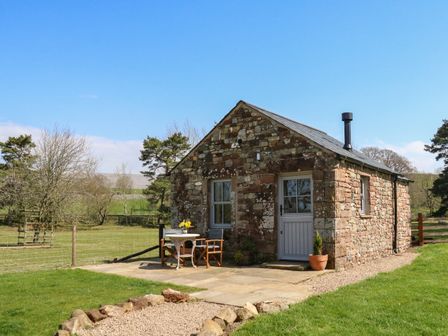 A stone cottage with a table and two chairs outside on a paved area at Herdie Hideaway in Appleby-In-Westmorland