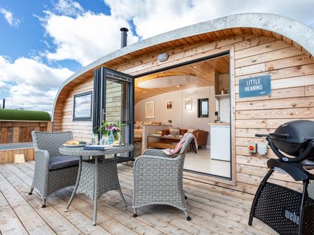 A wooden patio with table and chairs next to an open door to a living area at Little Heaning in Cartmel