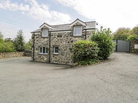 A stone house with shuttered windows a bush a driveway and a gate at The Coach House in Dolgellau