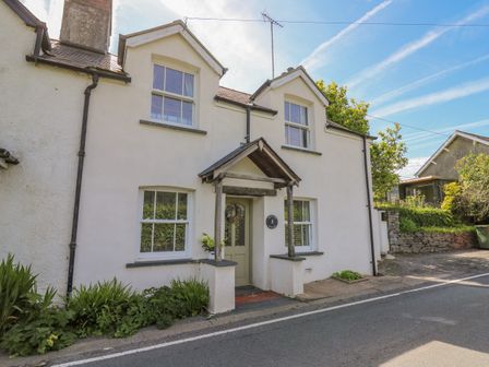 A white two-story cottage with two dormer windows and a small porch at Bryniau Bychain Cottage in Pennal near Cwrt