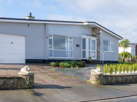 A single-story house with a garage and plants in the front garden at Cartref in Benllech