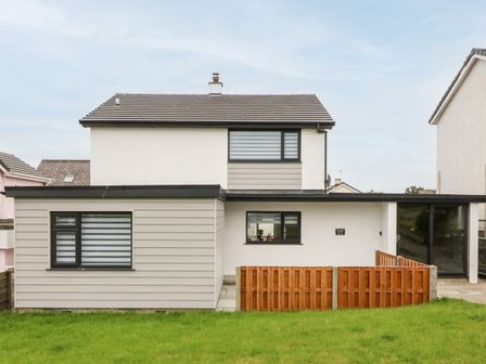 A two-story house with white and beige exterior walls a wooden fence and a grass lawn at Daresfield in Cemaes Bay