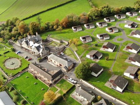 An aerial view of a residential area with multiple small houses surrounding larger buildings and green fields at Harcombe House Bungalow 11 in Chudleigh