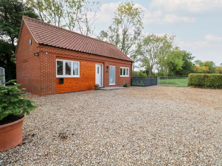 A brick house with a tiled roof and a gravel driveway with trees and a metal gate at Robins Nest in Brisley near North Elmham