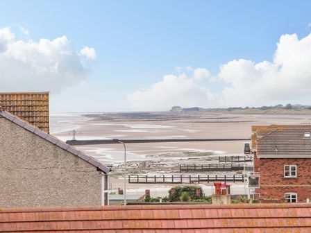 A view of rooftops and a sandy beach with groynes under a blue sky at Ty Uchaf in Rhyl