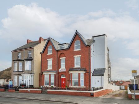 A red brick building with a red door and multiple windows beside a three-story beige building at Ty Canol in Rhyl