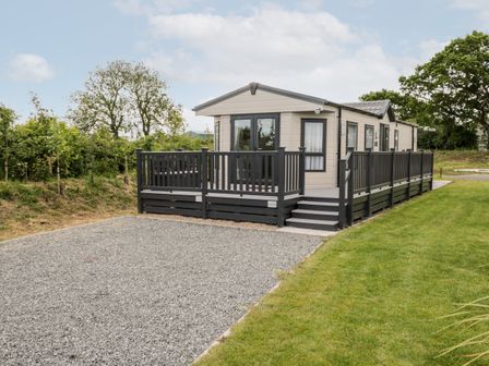 A modern static caravan with a wooden deck and gravel driveway surrounded by grass and trees at Lazy Daze Carnaby near Bridlington