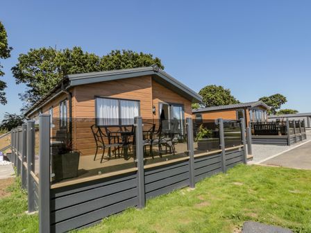 Two wooden lodges with glass fenced patios and outdoor furniture on a grassy area at Brighter Daze in Carnaby near Bridlington