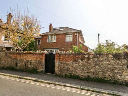 A two-story brick house behind a stone and brick wall with a black gate and a tree nearby at The Nook in Weymouth
