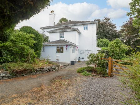 A white two-story house with a chimney surrounded by greenery and a wooden gate at Pentre Court Cottage in Abergavenny