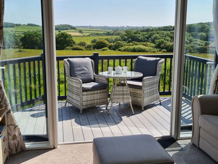A balcony with two chairs and a table with cups and teapot overlooking green fields at Vendee Lodge Thorness Bay Holiday Park near Cowes