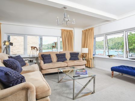 A living room with beige sofas blue cushions glass coffee table and large windows overlooking water at 2 Lee Court in Dartmouth