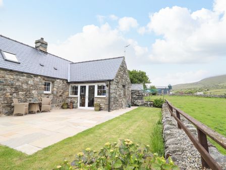 An outdoor patio area with chairs and a table beside a stone house with a slate roof and lawn at Caerffynon Bach in Dyffryn Ardudwy