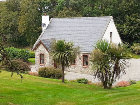 A stone cottage with a slate roof surrounded by grass and palm trees at Cornode Cottage in Garrykennedy County Tipperary